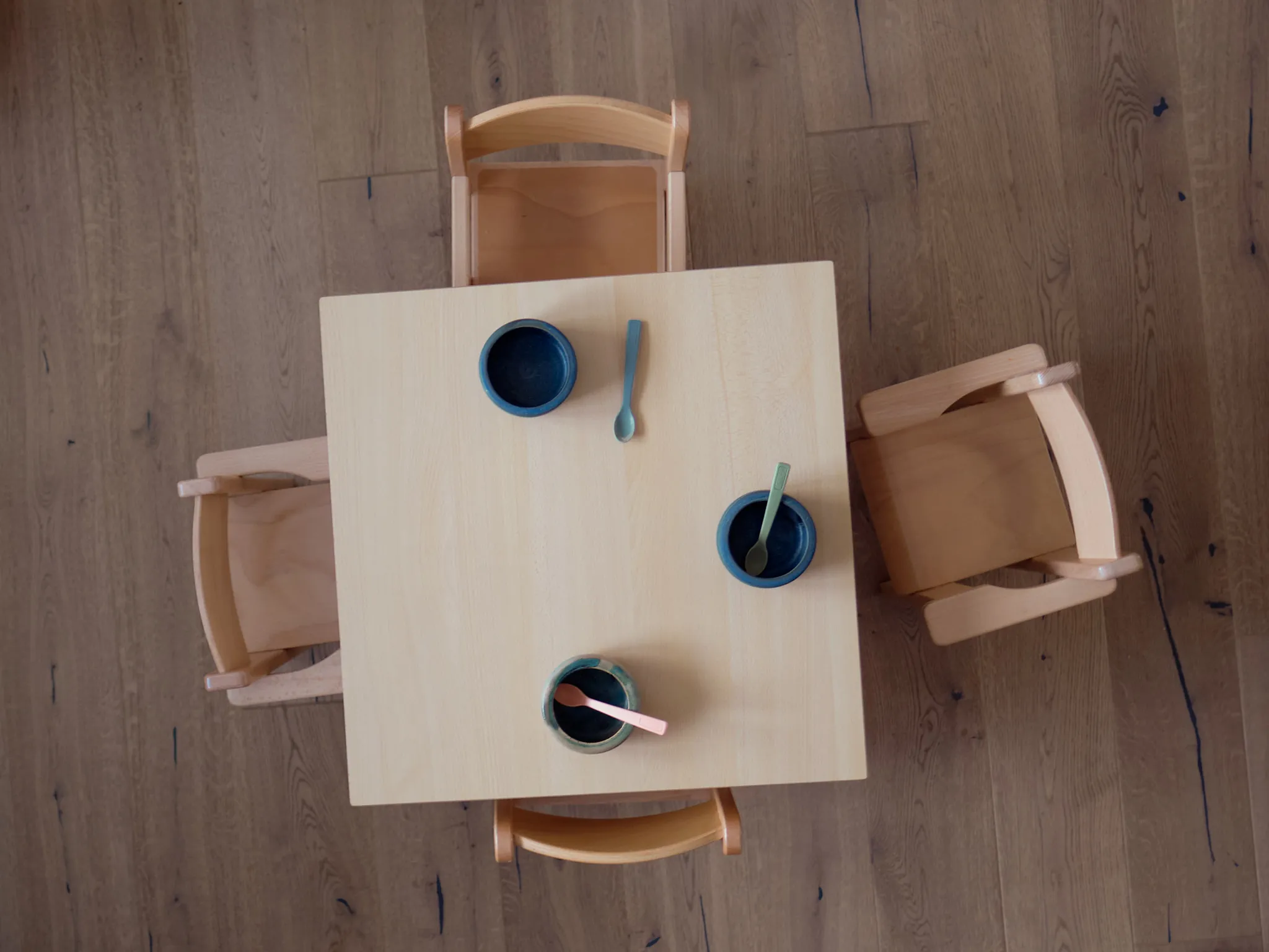 Kleiner Holztisch mit drei Schalen und Löffeln, umgeben von Kinderstühlen.