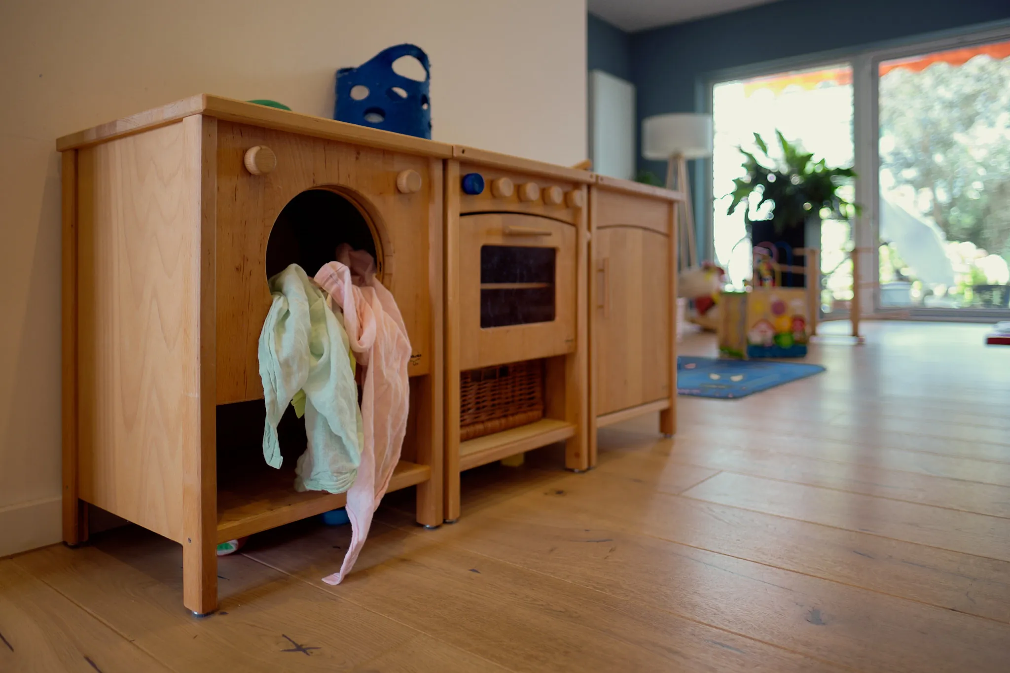 Spielküche aus Holz mit bunten Tüchern im lichtdurchfluteten Betreuungsraum.